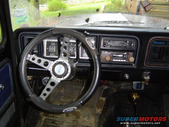 1979 Ford Bronco interior showing aftermarket steering wheel, dashboard gauges, and dual DIN radios
