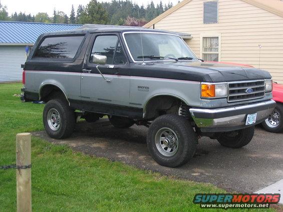 Lifted two-tone gray and black Ford Bronco with chrome wheels and a lifted suspension, parked on a gravel driveway