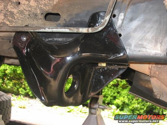 Close-up of a black suspension bracket bolted to a vehicle frame, with a tire visible at the bottom left