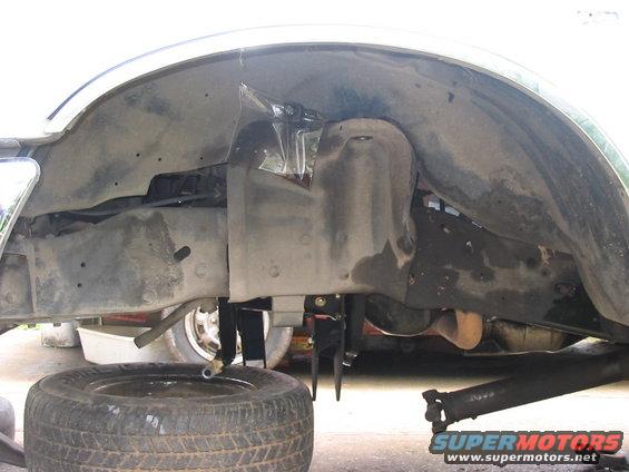 Underside of a vehicle showing the wheel well, suspension components, and a removed tire