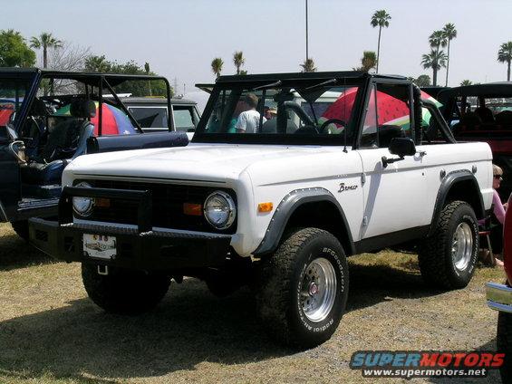 White first-generation Ford Bronco with black roll cage and aftermarket bumper