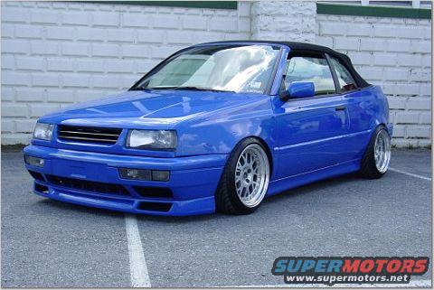 Blue convertible sports car with aftermarket body kit and wheels parked on asphalt