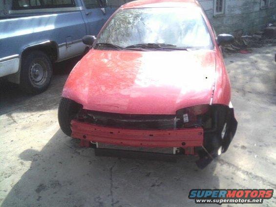 Red car with missing front bumper and grille, parked next to a blue pickup truck