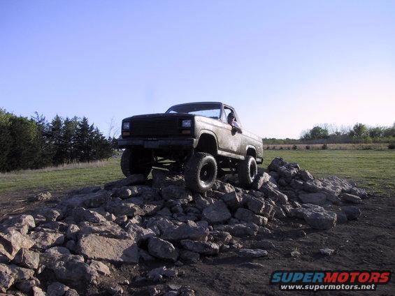 Brown lifted pickup truck on rocks, front 3/4 view, clear sky