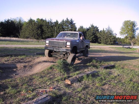 Ford pickup truck with lifted suspension driving on an off-road course. Grille suggests early 1980s