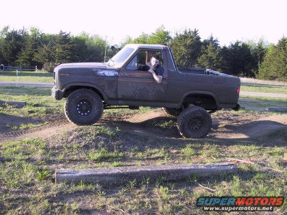 Muddy 1980s Ford Bronco with lifted suspension driving over dirt mounds