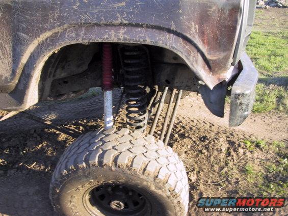 close-up of a lifted off-road vehicle's rear suspension and tire, showing a red shock absorber and coil spring