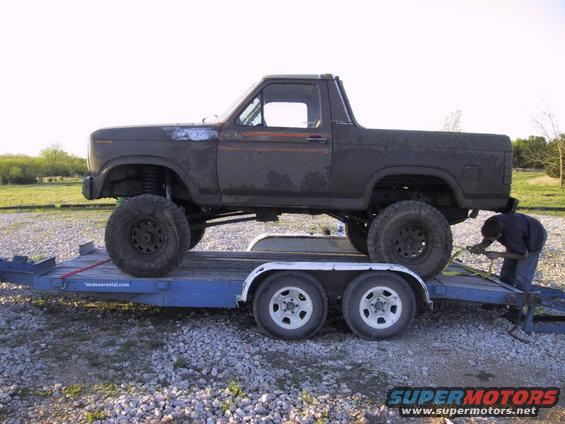 Lifted Bronco on a trailer, someone is strapping it down