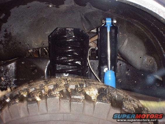 Suspension components including a black coil spring and a blue shock absorber, viewed from below the wheel well
