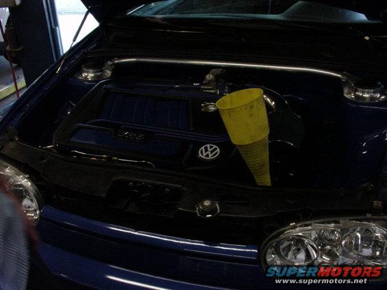 Blue 1998 Volkswagen Jetta engine bay with a yellow funnel inserted into the engine