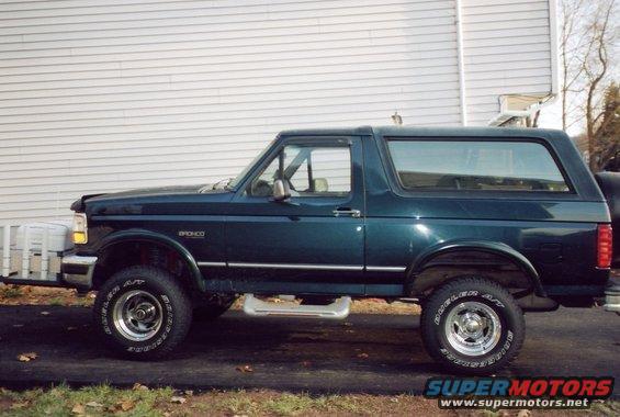 1994 Ford Bronco, side view, dark green paint, parked on asphalt in front of a white sided house