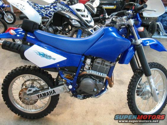 Blue Yamaha dirt bike with white decals on the side, parked indoors with other vehicles behind it