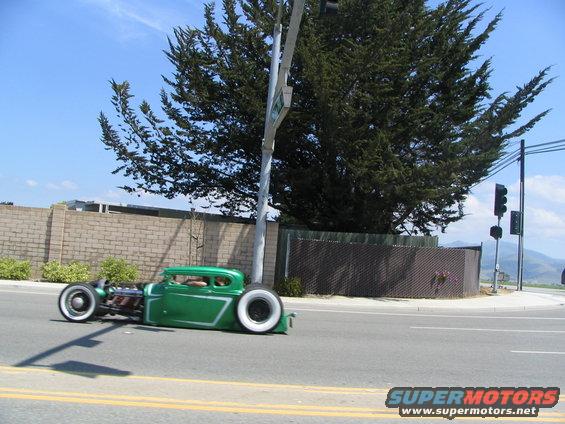 Green hot rod coupe with white wall tires and custom side trim, driving on a road