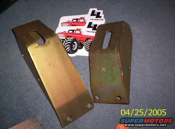 Two gold-colored metal brackets with holes, next to two stickers of red monster trucks. Date stamp 04/25/2005