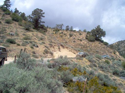 Two trucks on a dusty hillside road, one white pickup and one blue SUV