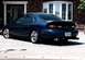 1999 Ford Taurus - A blue 1999 Ford Taurus sedan is parked outside a brick building, viewed from the rear.