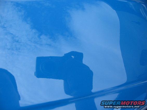 Camera reflected on a shiny blue surface, possibly a car hood