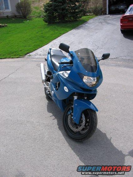 Blue sport motorcycle parked on asphalt driveway, front view. Dual headlights, dark windscreen, silver exhaust pipe