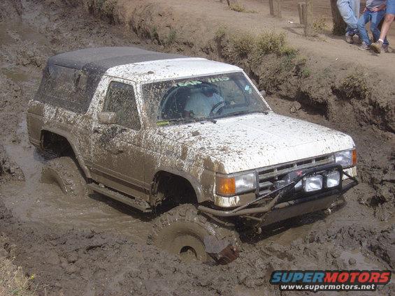 White SUV stuck in mud, front bumper with lights visible. Text 'TEAM THIS' on windshield