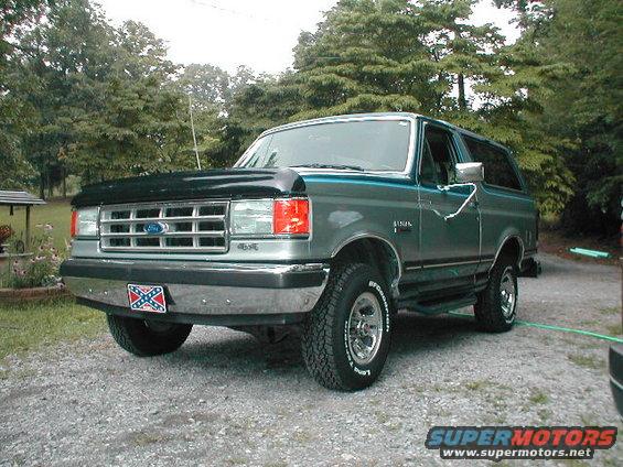 Ford Bronco with a black hood and teal stripe, parked on gravel