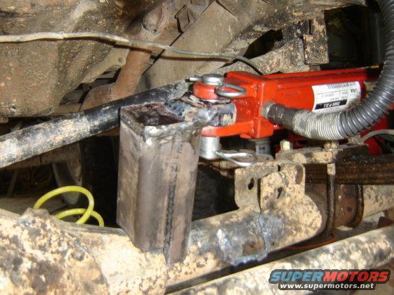 Modified suspension component with red hydraulic cylinder attached to rusty metal