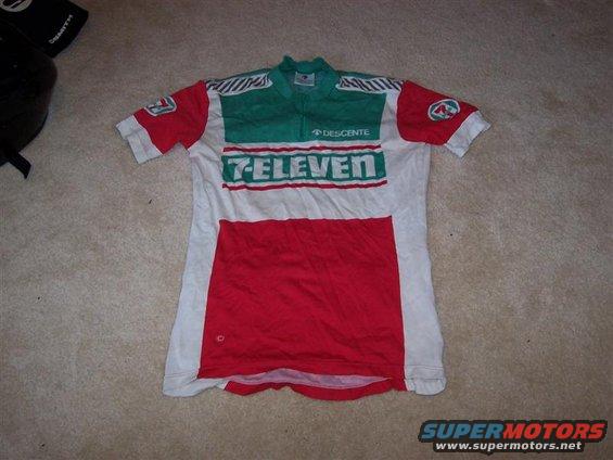 Red, white, and green 7-Eleven cycling jersey with Descente logo, laid flat on carpet