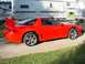1999 Mitsubishi 3000GT - A red sports car with a distinctive rear spoiler is parked on a concrete surface.