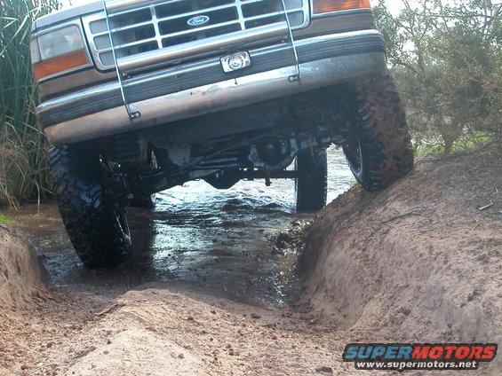 1992 Ford F-150 front end angled down a muddy incline into water, showing grille and tires
