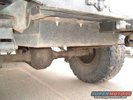Underside of a vehicle showing the rear axle, differential, and a large fuel tank mounted above it. A tire is visible on the right