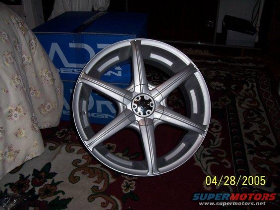 Silver five-spoke aftermarket wheel with black accents, resting on a patterned rug