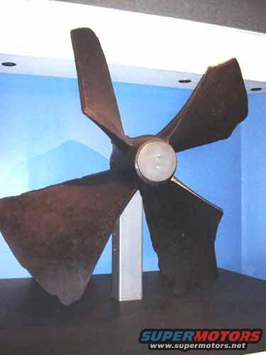 Brown four-bladed propeller mounted on a stand against a blue wall