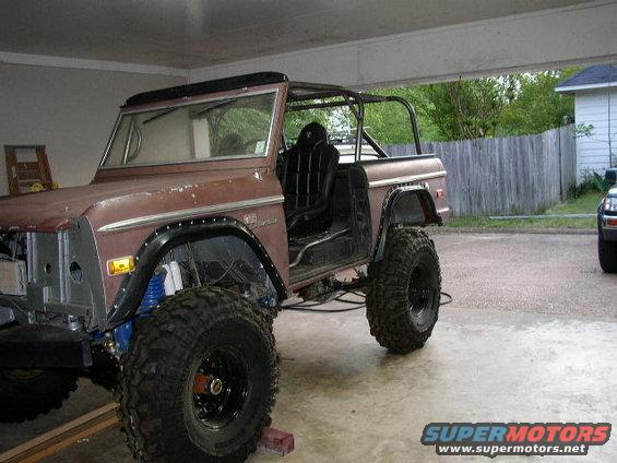 Brown Ford Bronco with roll cage and large tires, doors removed, in a garage