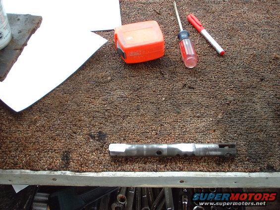 Metal rod with holes, tape measure, screwdriver, and marker on carpeted surface