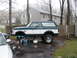 1994 Ford Bronco - A two-tone Ford Bronco is elevated on jack stands in a driveway, undergoing maintenance.
