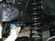 1994 Ford Bronco - A hand holds a black suspension bushing near the coil spring and frame of a vehicle.