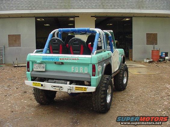 Teal and white Ford Bronco with roll cage and large tires, viewed from rear