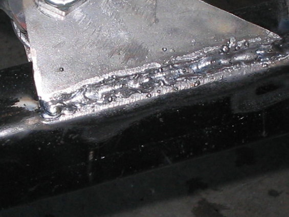 Close-up of a rough weld on a silver metal bracket attached to a black metal frame
