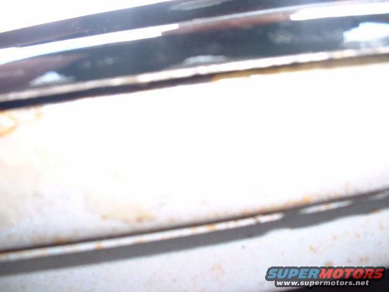 Close-up of chrome trim above a white panel with some rust spots. Supermotors.net logo visible