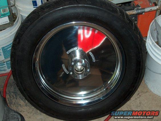 Chrome motorcycle wheel with tire, showing reflection of red and white sign