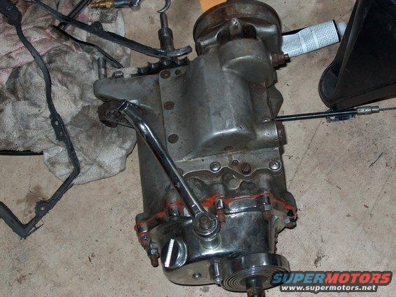 motorcycle transmission with shift lever and cable attached, on a concrete floor with rags