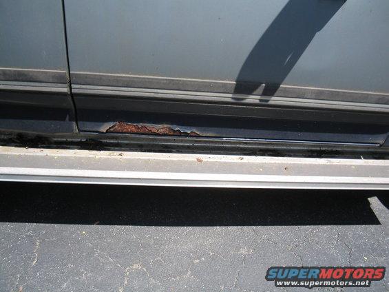Close-up of a vehicle's side showing rust on the rocker panel below the trim