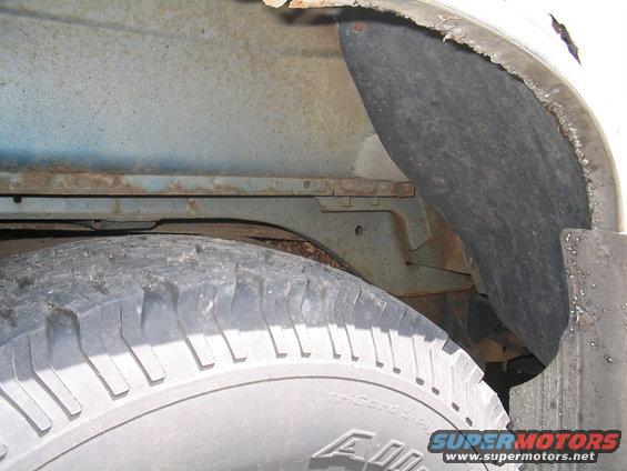 Close-up of rusty frame and wheel well liner with tire visible