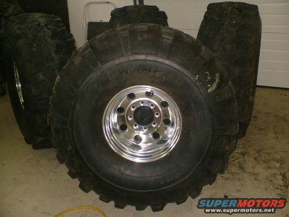 Four large off-road tires with chrome rims stacked in a garage