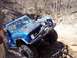 1995 Ford F-250 - A blue first-generation Ford Bronco navigates a challenging muddy terrain with large off-road tires.