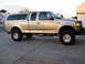 1999 Ford F-150 - A gold 1999 Ford F-150 pickup truck is shown from the side, equipped with a camper shell and lifted suspension.