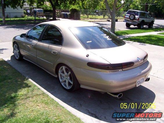 Tan sedan parked on driveway, with a Bronco in the background. License plate SCH779