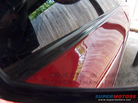 Reflection of a wooden fence in a car's side mirror and on its red door