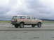 1988 Ford C-250 (Centurion Conversions) - A tan Ford Bronco Centurion Conversion sits on a sandy beach under a cloudy sky.