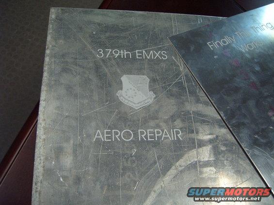 Metal plaque with '379th EMXS' and 'AERO REPAIR' text, plus an emblem. Another metal sheet is partially covering it
