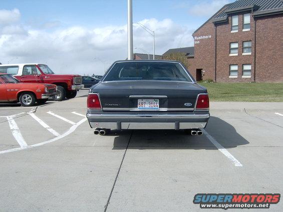 1990 Ford Crown Victoria rear view, parked next to a red pickup truck and an orange car